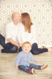 Best-Family-Photographer-Brentwood-Studio-Portrait-Session-Focus-On-Baby-Parents-Kissing-In-Background