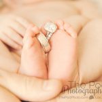 close up photo of mom and dads rings on newborn baby's toes