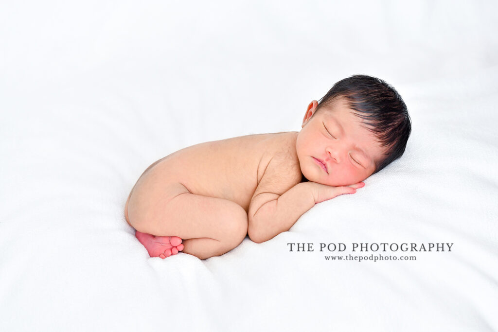 Newborn baby boy sleeping and posed on a white blanket.